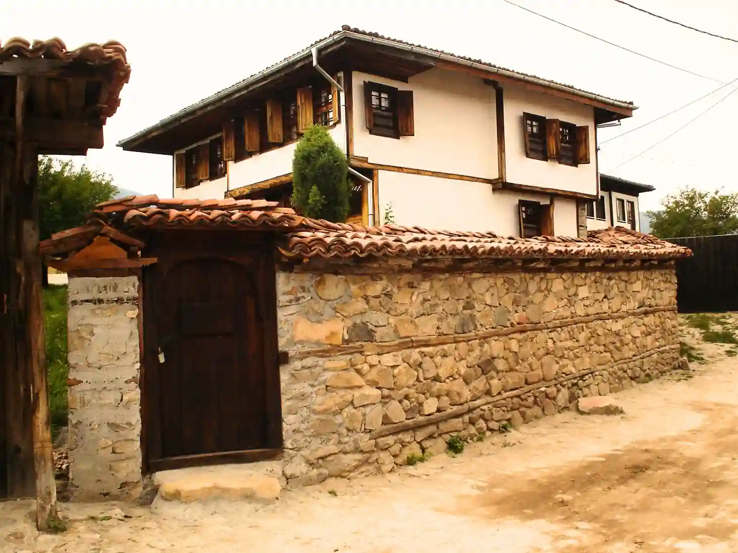Historic Property with Stone Wall and Wooden Gate Authentic Bulgarian house in Koprivshtitsa with a white facade, wooden beams, and traditional architecture.