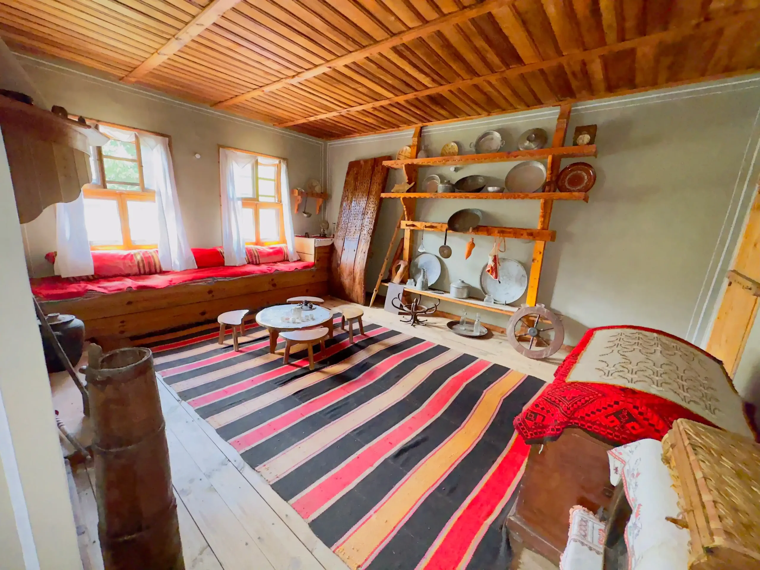 Vestibule-of-a-house-in-Koprivshtitsa Indoor seating area with wooden chairs and a colorful rug in the courtyard of a historic Bulgarian house.